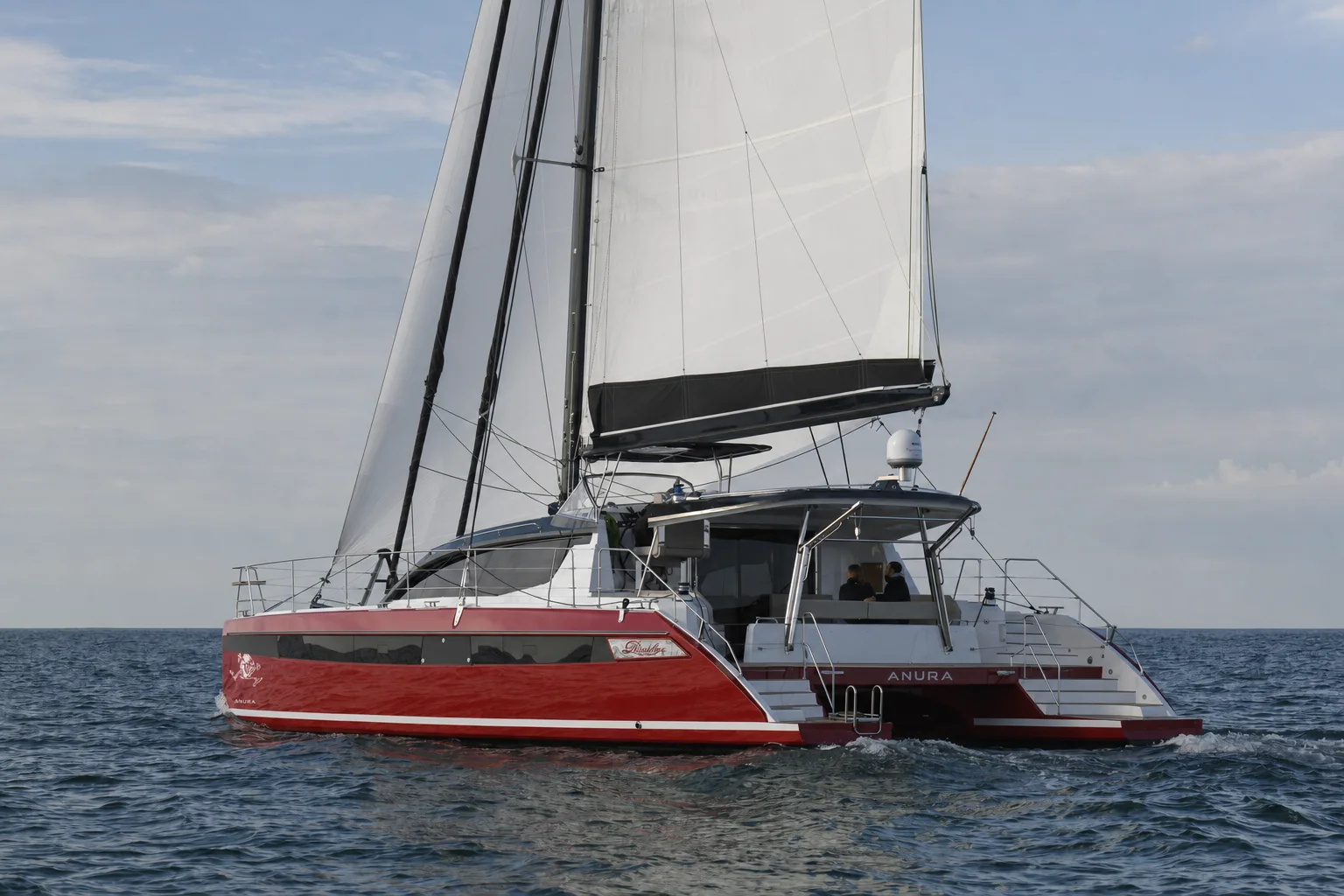 ANURA, a red-hulled Privilege 510 catamaran, under full sail